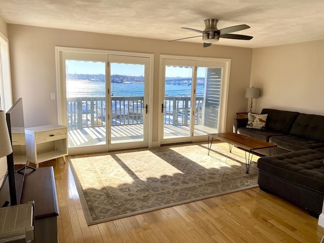 living room with hardwood / wood-style flooring, a water view, and ceiling fan