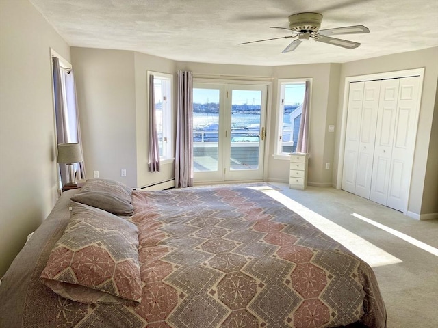 carpeted bedroom with a baseboard heating unit, a closet, ceiling fan, and a water view