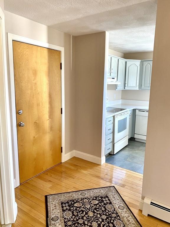 kitchen featuring a baseboard radiator, white cabinets, white appliances, a textured ceiling, and light wood-type flooring