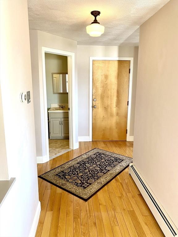 corridor featuring a baseboard heating unit, sink, hardwood / wood-style floors, and a textured ceiling