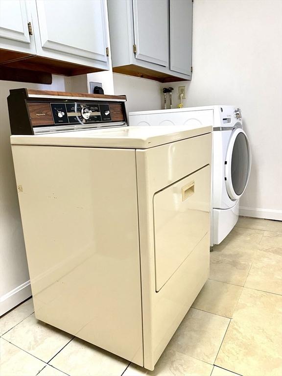 laundry area with light tile patterned floors, washer and clothes dryer, and cabinets