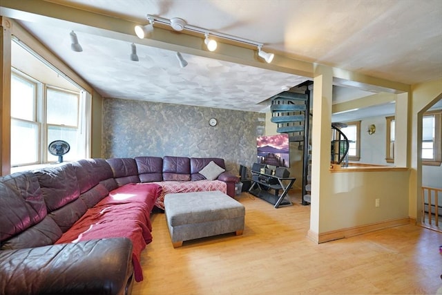 living area with wood finished floors, wallpapered walls, track lighting, baseboards, and an accent wall