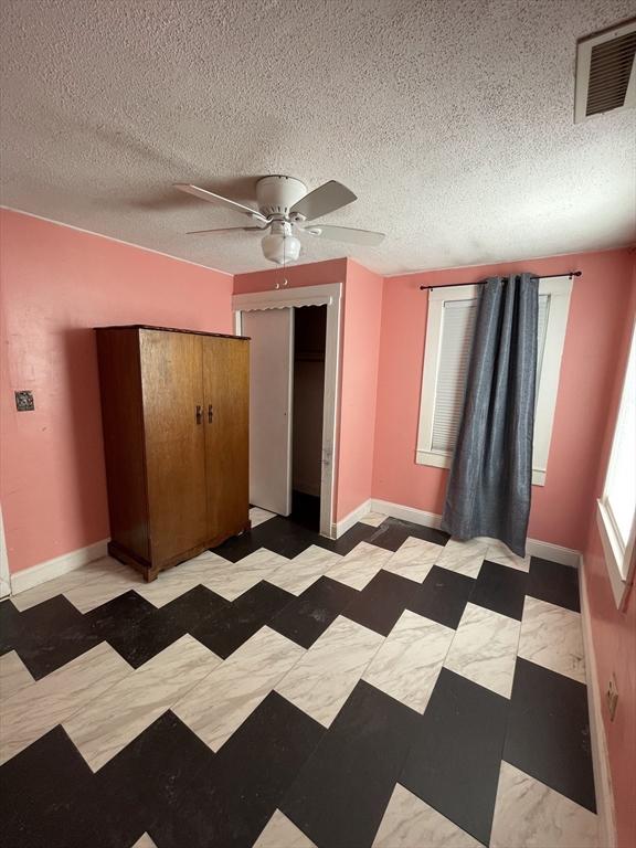 unfurnished bedroom with a textured ceiling, ceiling fan, and a closet