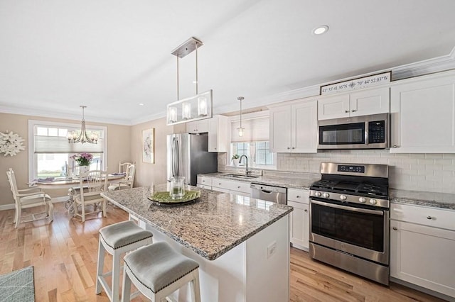 kitchen featuring stainless steel appliances, hanging light fixtures, light stone countertops, a kitchen island, and white cabinetry