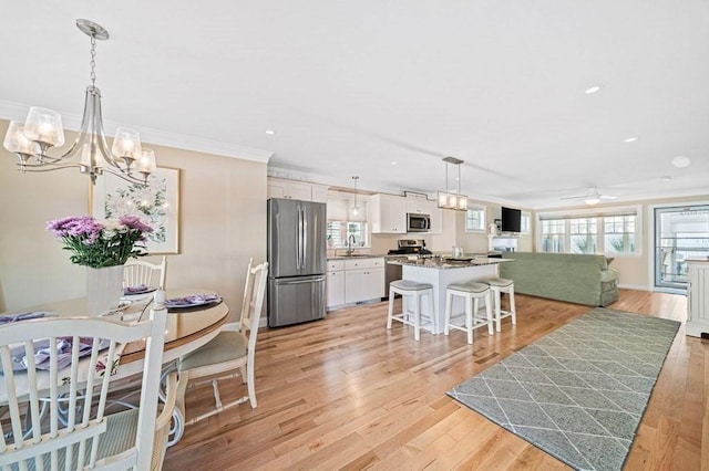 kitchen featuring hanging light fixtures, stainless steel appliances, a breakfast bar, crown molding, and white cabinets