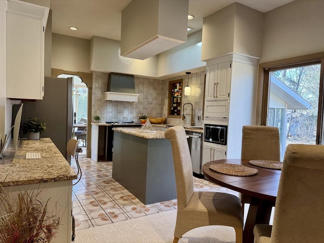 kitchen featuring white cabinets, a center island, stainless steel appliances, wall chimney range hood, and backsplash