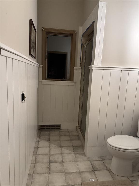 bathroom with toilet, a stall shower, wainscoting, and visible vents