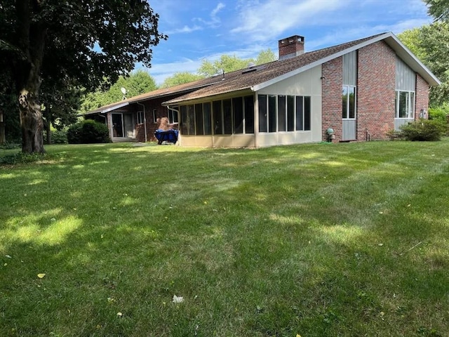 rear view of house with a sunroom, brick siding, a yard, and a chimney