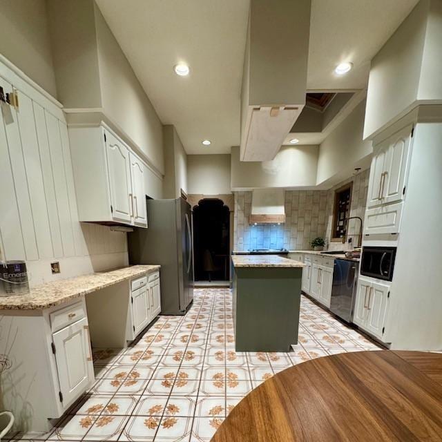 kitchen featuring a kitchen island, white cabinetry, wall chimney range hood, appliances with stainless steel finishes, and tasteful backsplash