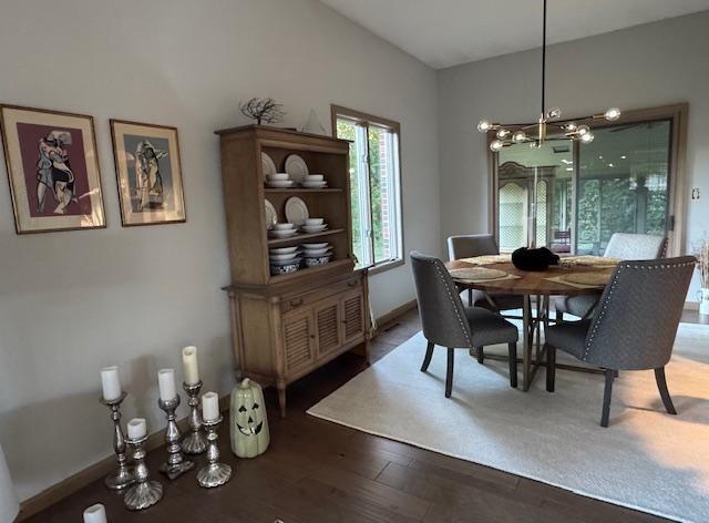 dining area with a notable chandelier, vaulted ceiling, baseboards, and wood finished floors