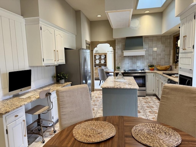 kitchen featuring a center island, stainless steel appliances, tasteful backsplash, built in study area, and wall chimney exhaust hood