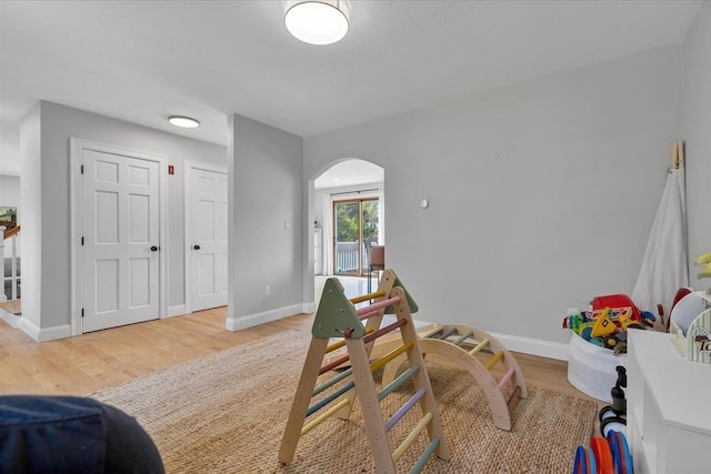 rec room featuring arched walkways, light wood finished floors, and baseboards