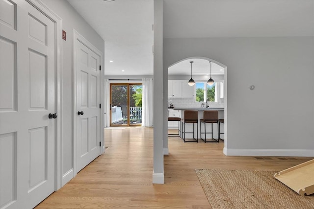 hallway with arched walkways, light wood finished floors, recessed lighting, and baseboards