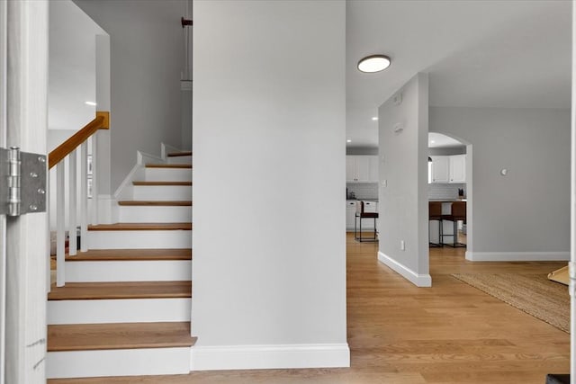 staircase featuring arched walkways, wood finished floors, and baseboards