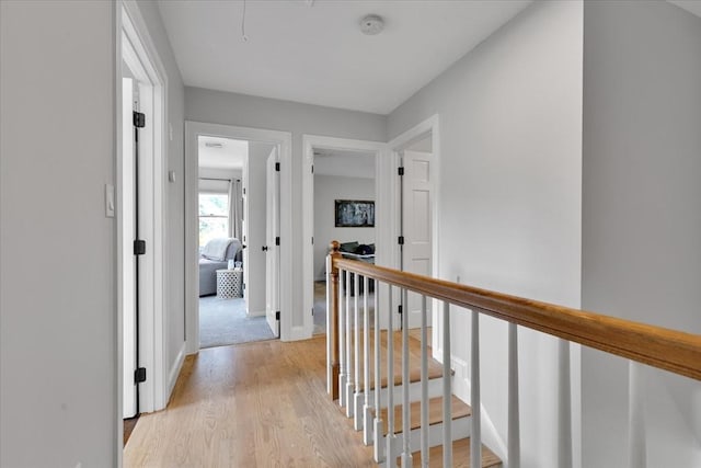 corridor with an upstairs landing, light wood-style flooring, and baseboards