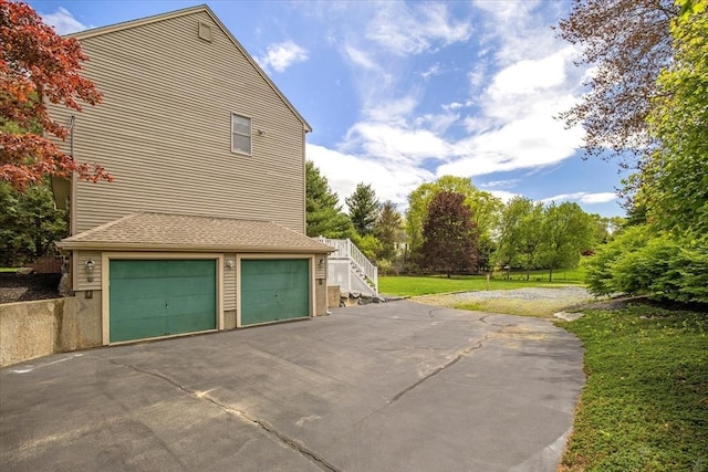 view of side of property featuring asphalt driveway, an attached garage, and a lawn