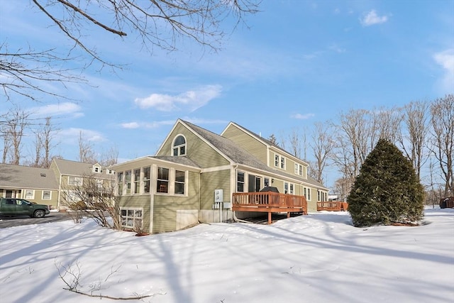 snow covered house with a wooden deck and a sunroom