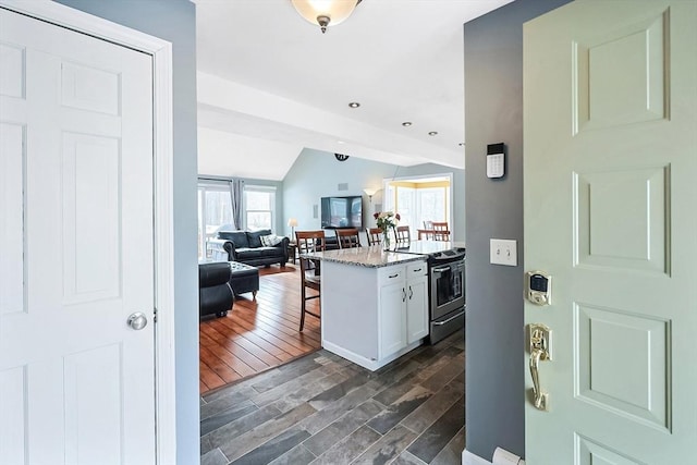 kitchen with white cabinets, electric stove, lofted ceiling, a breakfast bar, and dark wood-type flooring