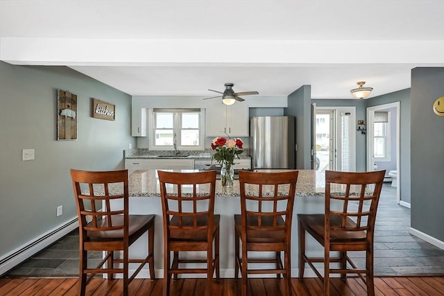 dining space featuring a baseboard heating unit, dark wood-style flooring, ceiling fan, and baseboards