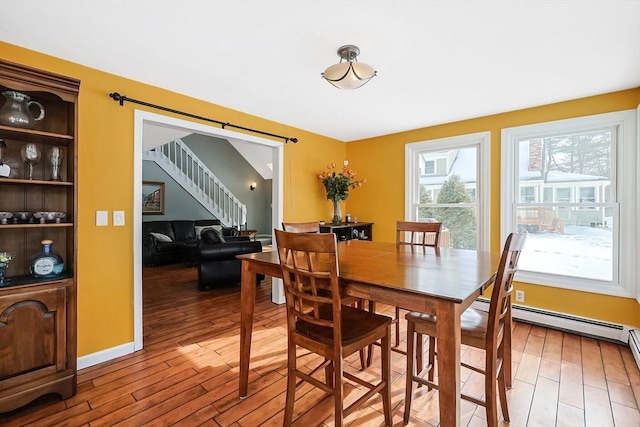 dining room with baseboard heating, wood finished floors, baseboards, and stairs