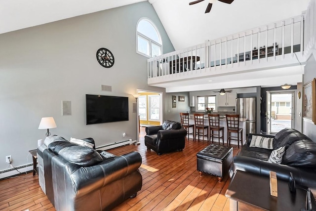 living area featuring light wood-style floors, a baseboard heating unit, and a ceiling fan