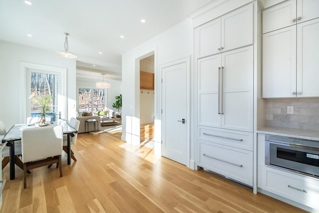 kitchen with hanging light fixtures, decorative backsplash, light hardwood / wood-style flooring, and white cabinets