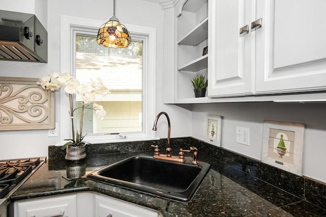 kitchen featuring dark stone counters, decorative light fixtures, white cabinetry, open shelves, and a sink