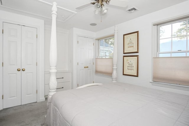 bedroom featuring ceiling fan, light colored carpet, visible vents, two closets, and attic access