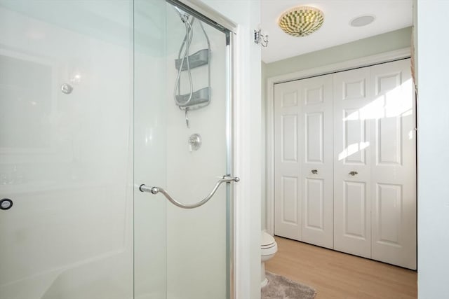 bathroom featuring a stall shower, a closet, toilet, and wood finished floors