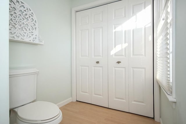 half bathroom featuring a closet, wood finished floors, toilet, and baseboards