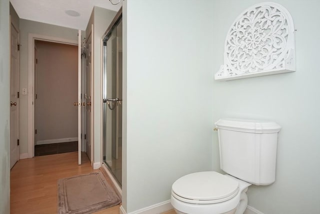 full bathroom featuring toilet, a stall shower, baseboards, and wood finished floors