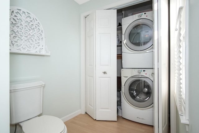 laundry area featuring laundry area, baseboards, light wood finished floors, and stacked washer / drying machine