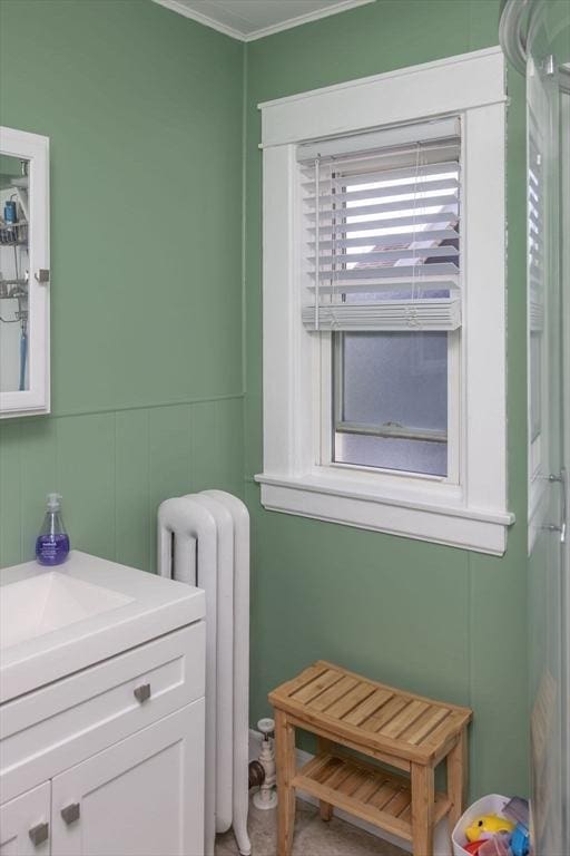 bathroom with radiator heating unit, vanity, crown molding, and a decorative wall