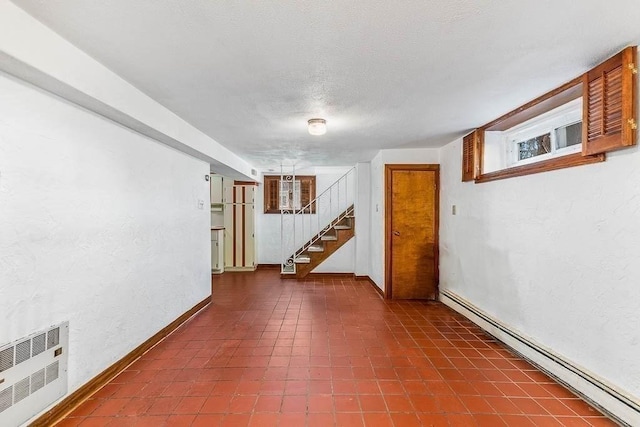 finished below grade area featuring a textured wall, radiator, baseboards, a baseboard heating unit, and stairway