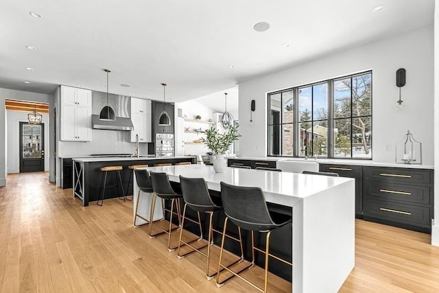 kitchen with a breakfast bar, pendant lighting, a large island, light hardwood / wood-style floors, and wall chimney range hood