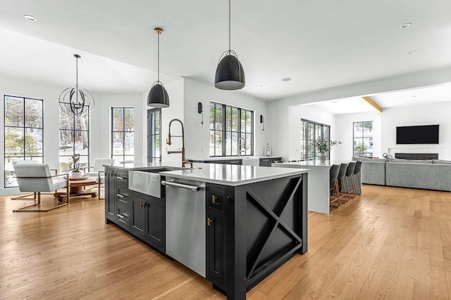 kitchen with sink, dishwasher, hanging light fixtures, light hardwood / wood-style floors, and a center island with sink