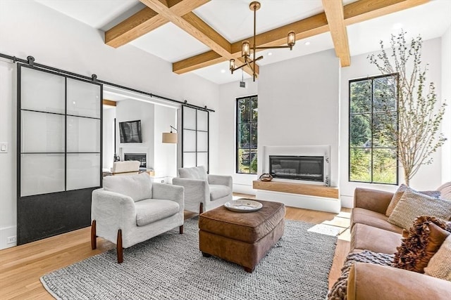 living room with coffered ceiling, a barn door, beam ceiling, and light wood-type flooring