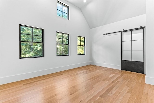 empty room featuring plenty of natural light, a barn door, high vaulted ceiling, and light wood-type flooring