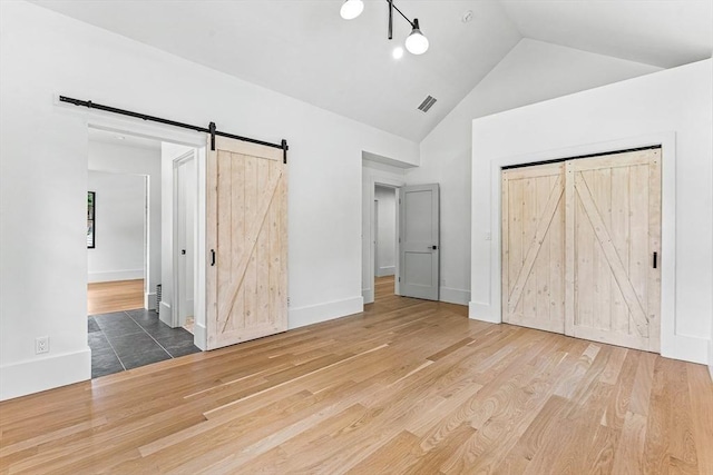 unfurnished bedroom with high vaulted ceiling, a barn door, hardwood / wood-style floors, and a closet