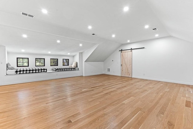 additional living space with vaulted ceiling, a barn door, and light hardwood / wood-style floors