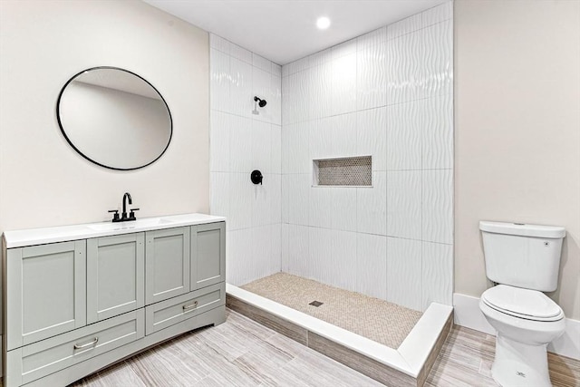 bathroom featuring vanity, a tile shower, and toilet