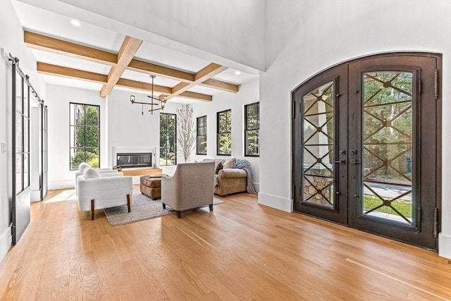 living room with beamed ceiling, coffered ceiling, a barn door, light wood-type flooring, and french doors