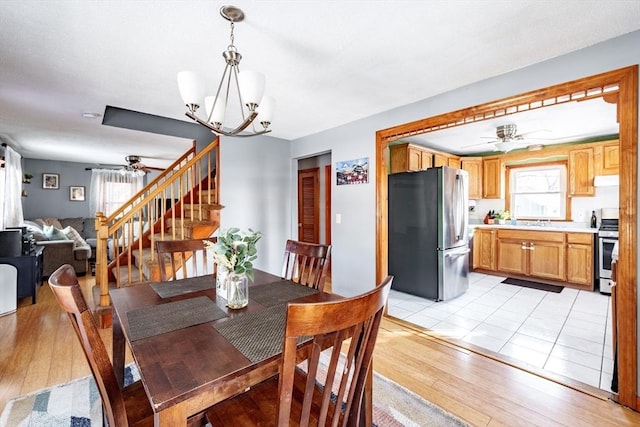 dining space with ceiling fan with notable chandelier, sink, and light hardwood / wood-style floors