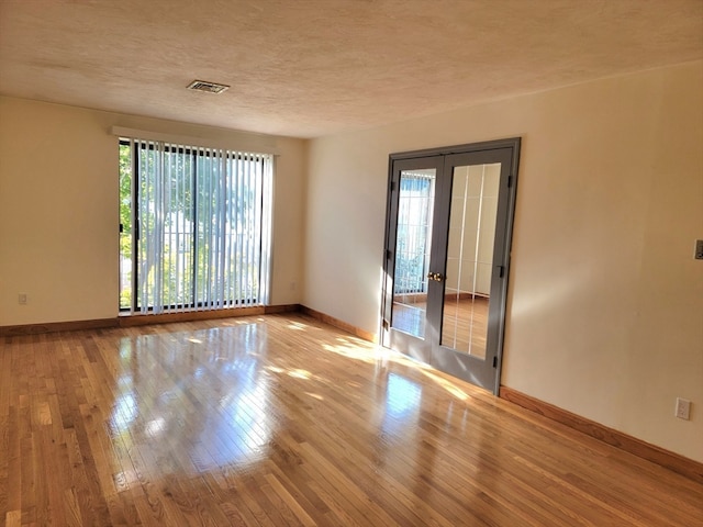 unfurnished room featuring a textured ceiling, french doors, plenty of natural light, and light hardwood / wood-style floors