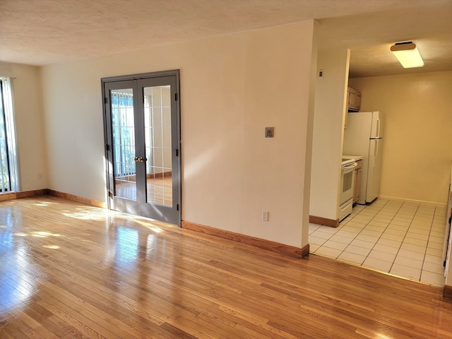 unfurnished room with french doors, light hardwood / wood-style floors, and a textured ceiling