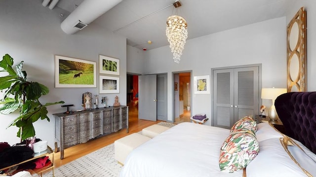 bedroom featuring visible vents, wood finished floors, a towering ceiling, and a chandelier