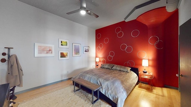 bedroom featuring an accent wall, lofted ceiling, wood finished floors, and baseboards