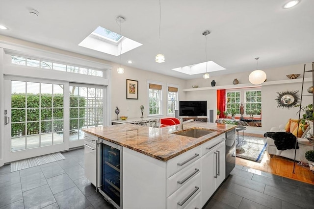 kitchen featuring sink, an island with sink, white cabinets, decorative light fixtures, and beverage cooler