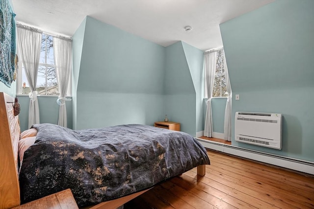 bedroom featuring hardwood / wood-style floors, a wall mounted AC, and baseboard heating