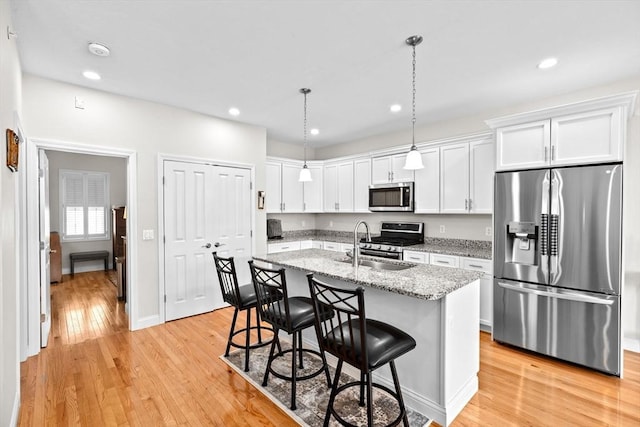 kitchen with light wood-style floors, a kitchen breakfast bar, white cabinetry, a sink, and appliances with stainless steel finishes